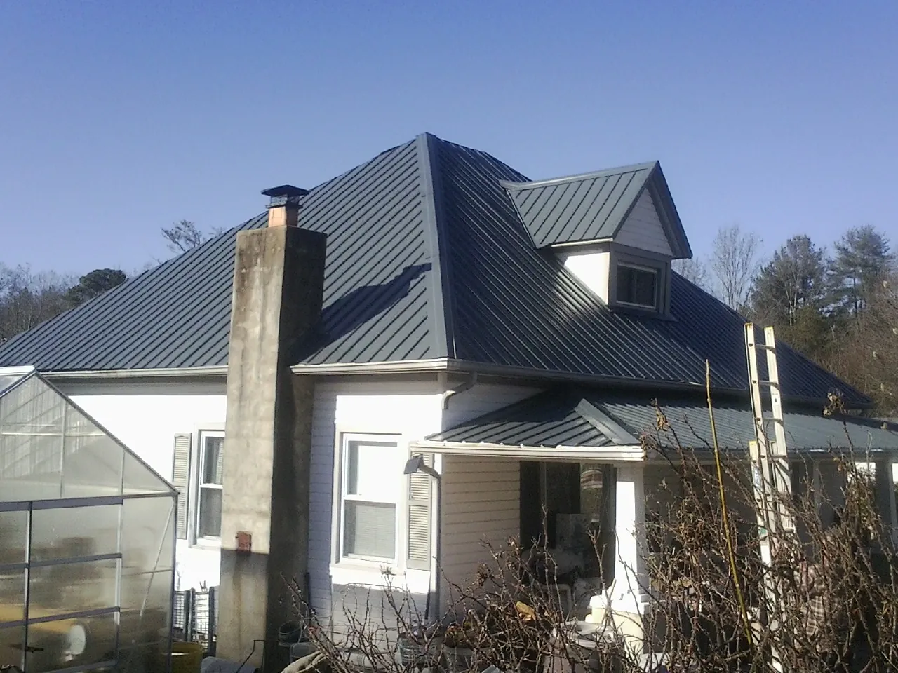 Dark blue standing seam metal roof on a white farmhouse with dormer — Slate & Tile Roof Repair by Roofing Brothers in White River Junction