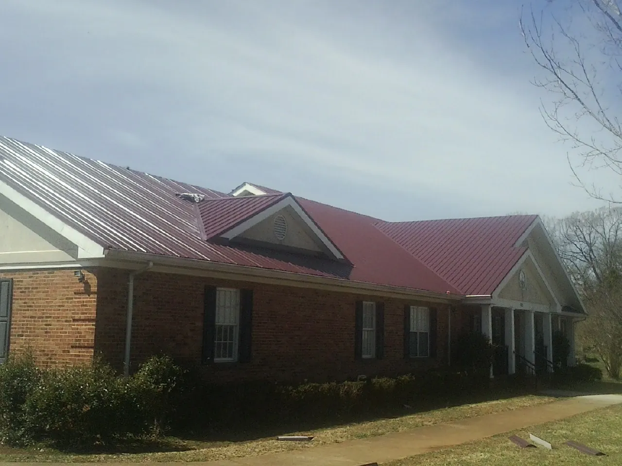 Red metal roof with gabled entries on a long brick building, from a Hail Damage Roof Repair job in White River Junction