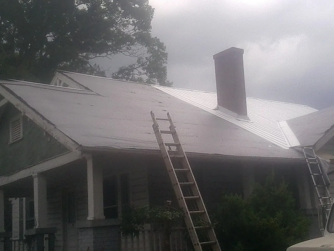 Ladders against a metal roof on an older home with a brick chimney in White River Junction