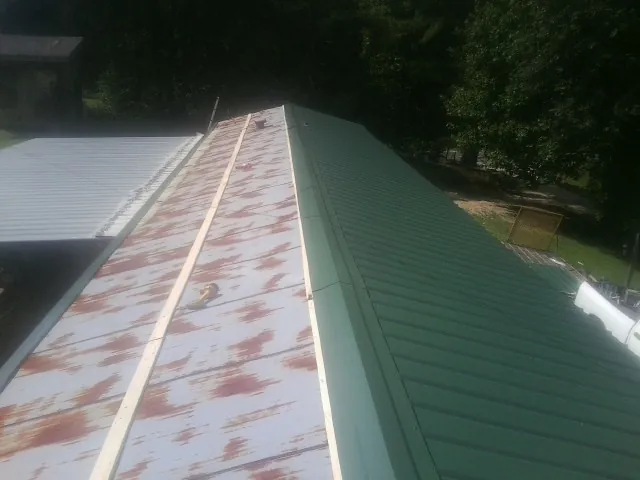 Old rusted panels beside newly installed green metal roofing — Wind Damage Roof Repair by Roofing Brothers in White River Junction