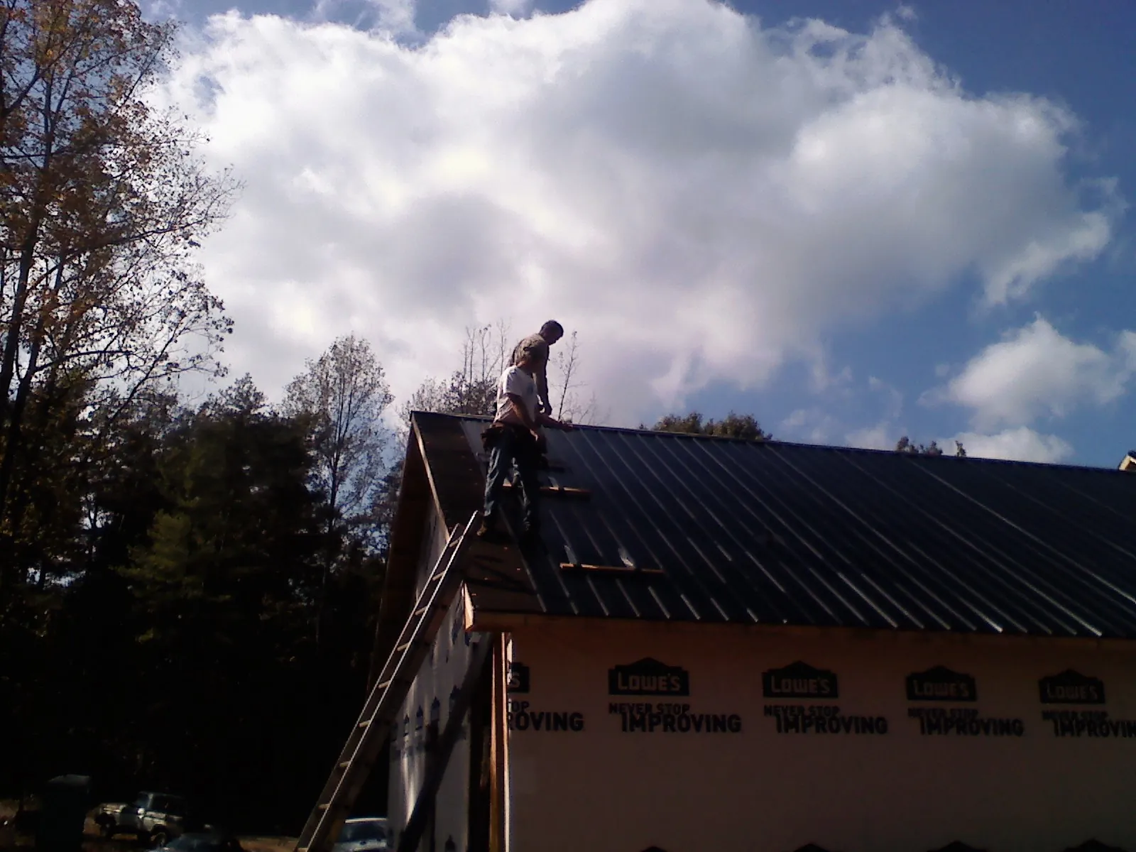 Roofer fastening dark metal panels high against a cloudy sky, from a Roof Inspection job in White River Junction