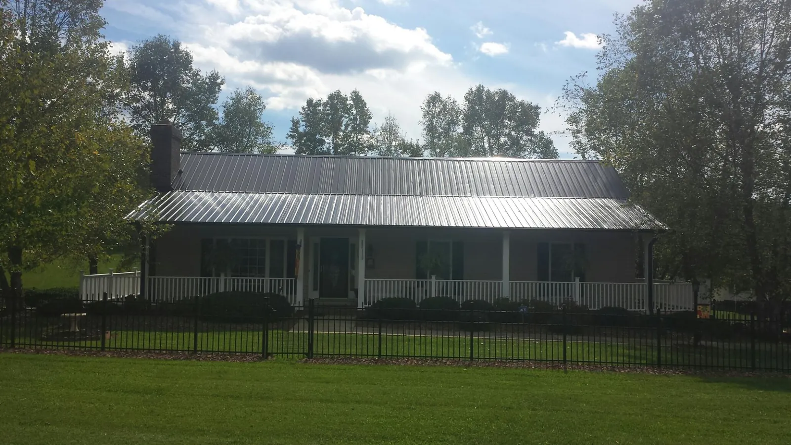 Gray metal roof on a brick ranch with a full width front porch — Gutter Guard Installation work by our crew in White River Junction