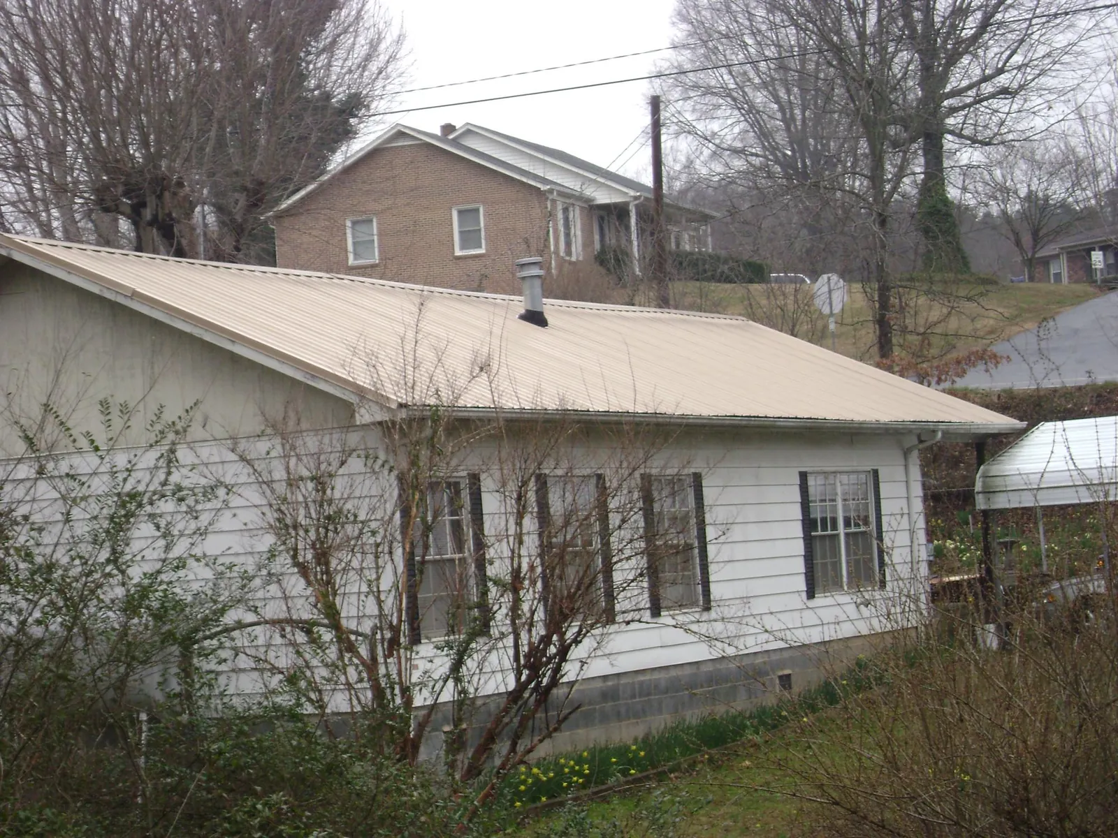 Tan metal roof on a white sided house set into a hillside — Commercial Roofing by Roofing Brothers in White River Junction